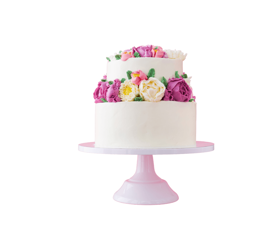 Dettaglio di una raffinata torta artigianale ricoperta di panna bianca, decorata con una fitta ghirlanda di fiori in crema nei toni del rosa, fucsia e bianco, presentata su un'alzata di colore rosa.